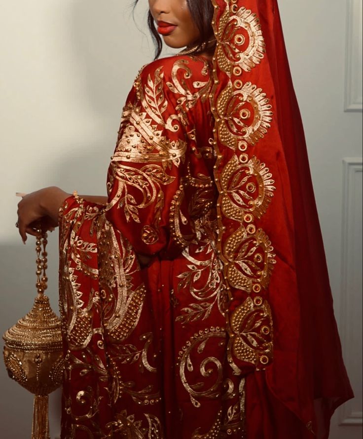 a woman in a red and gold dress holding a golden bell on her head while standing next to a white wall