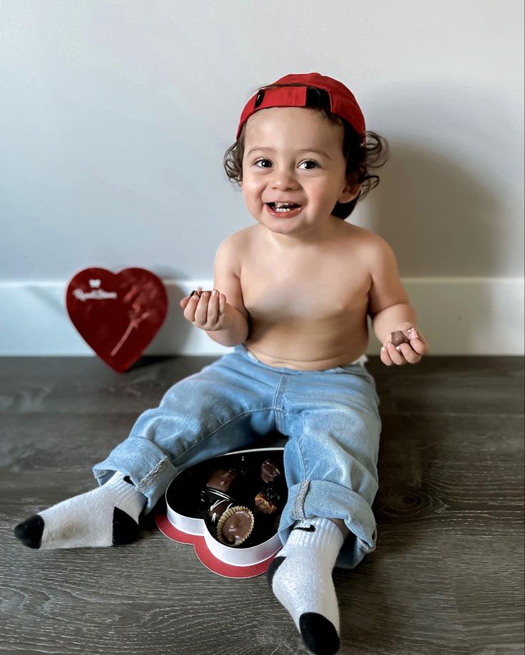 a small child sitting on the floor with some chocolates in his hand and smiling