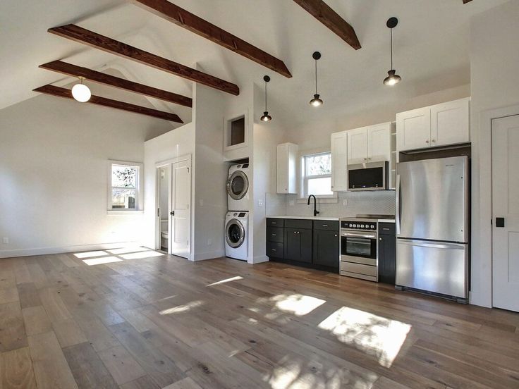 an empty kitchen and living room with wood floors, white walls and exposed ceiling beams