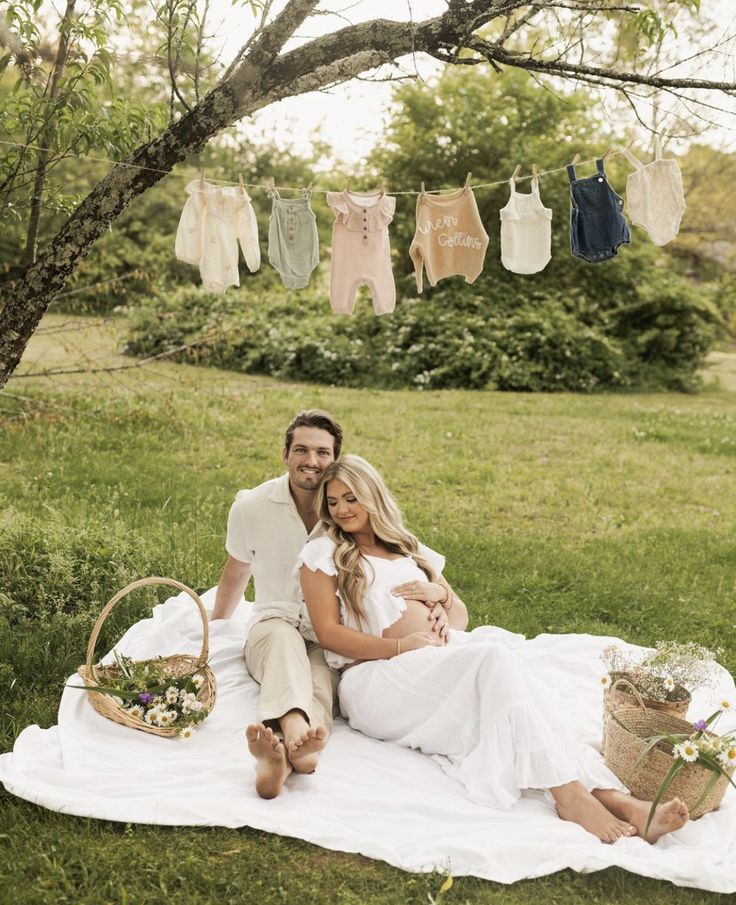 a pregnant couple sitting on a blanket in the grass