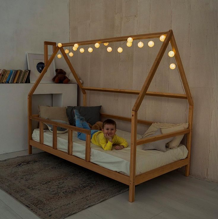 a little boy laying on top of a bed with lights strung from the ceiling above him