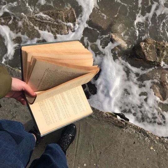 someone is holding an open book by the water