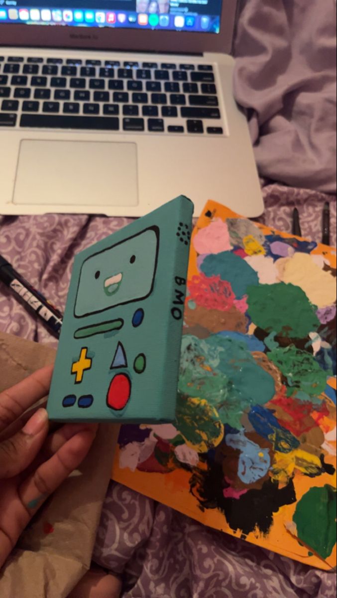 a person is holding a small box in front of a laptop and painting on paper