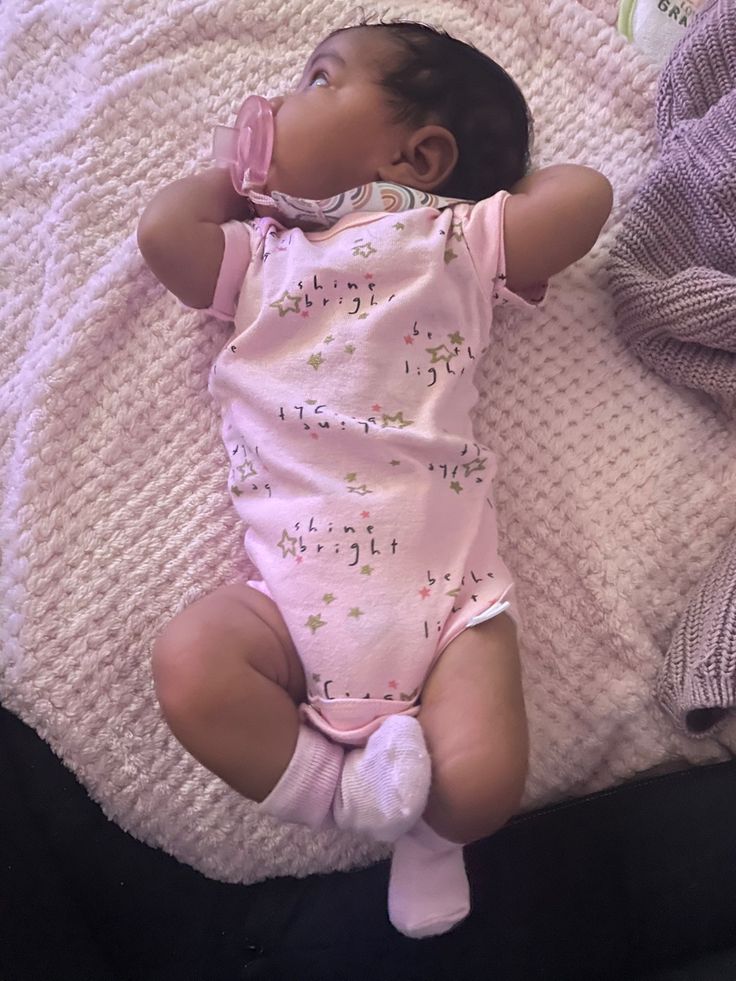 a baby laying on top of a bed next to a blanket