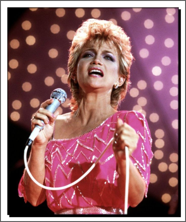 a woman singing into a microphone while wearing a pink dress and holding a white cord