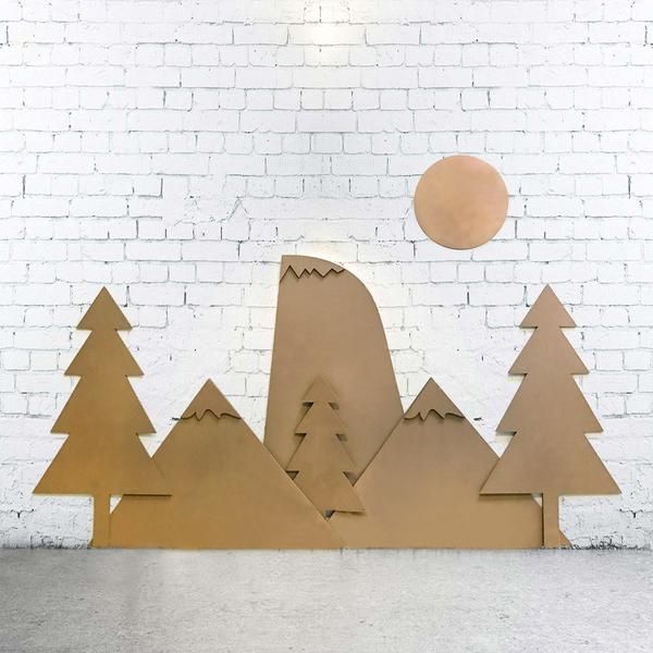 a wooden cutout of trees and mountains with a sun in the background on a white brick wall