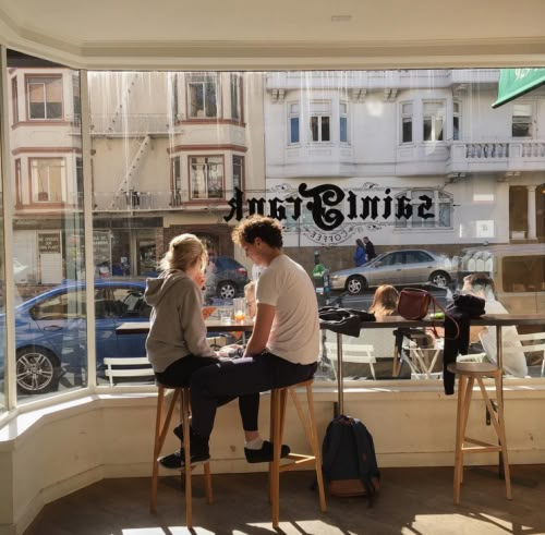 two people sitting at a table in front of a window with the words saint frank on it