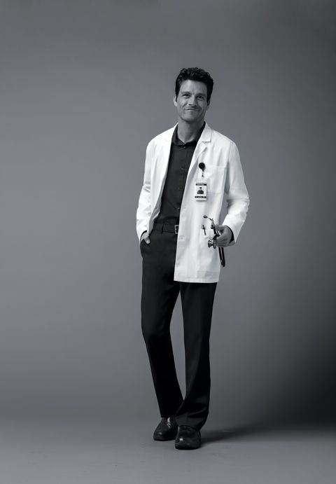 a male in a white lab coat and black pants is posing for a photo with his hands in his pockets