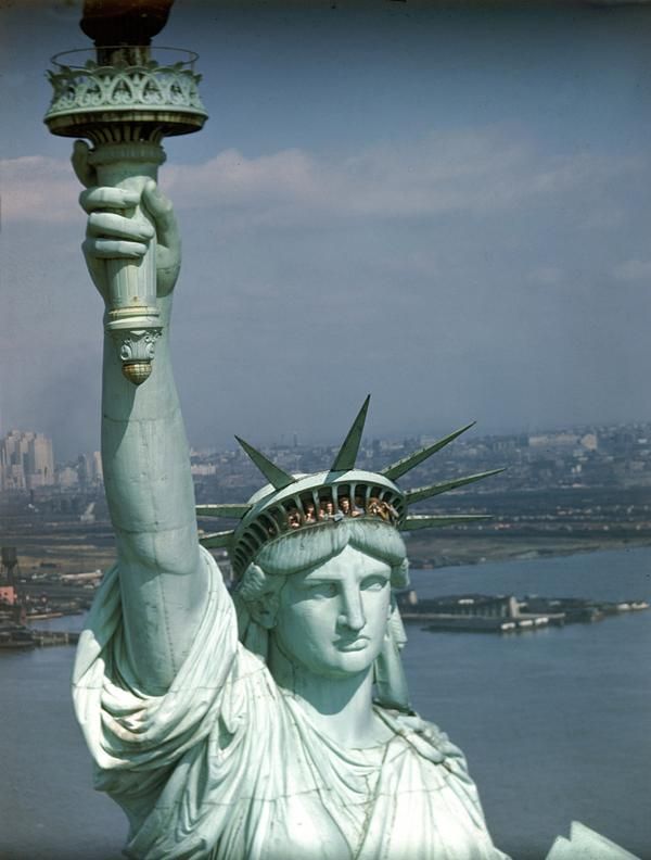 the statue of liberty is holding up a torch in her hand and looking down at the city