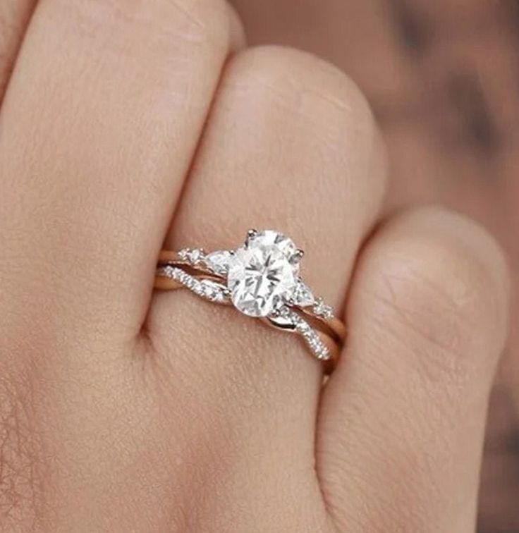 a woman's hand holding an engagement ring with two diamonds on the band and a diamond