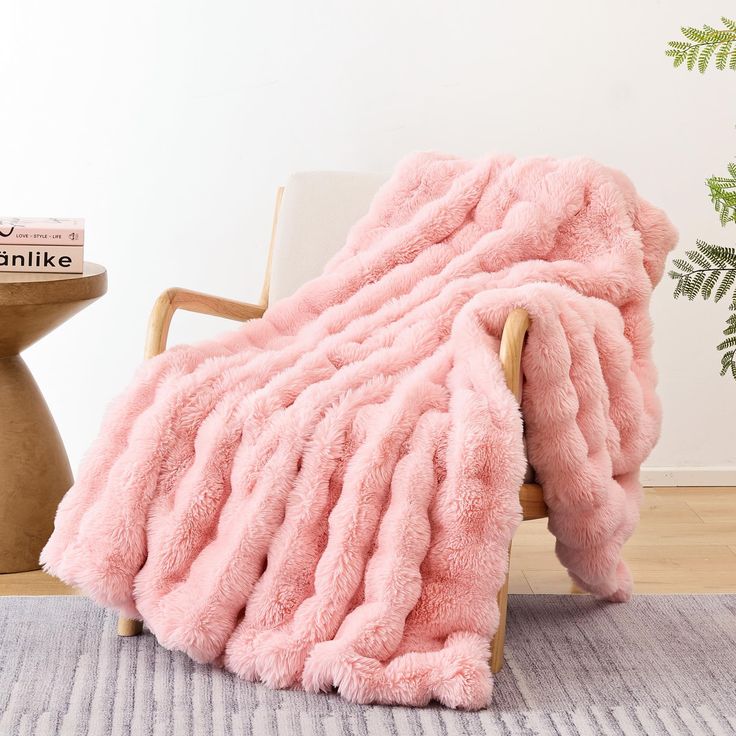 a pink blanket sitting on top of a wooden chair next to a white vase and potted plant