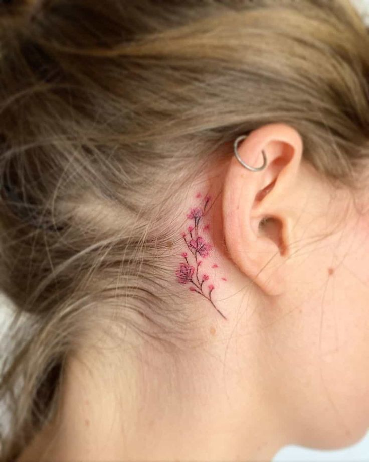 a woman's behind the ear has a small pink flower tattoo on her left side