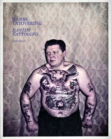 a man with tattoos standing in front of a wall