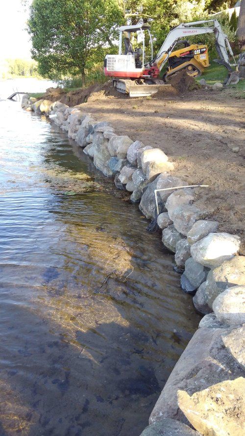 there is a construction truck parked next to the water and some rocks in the foreground