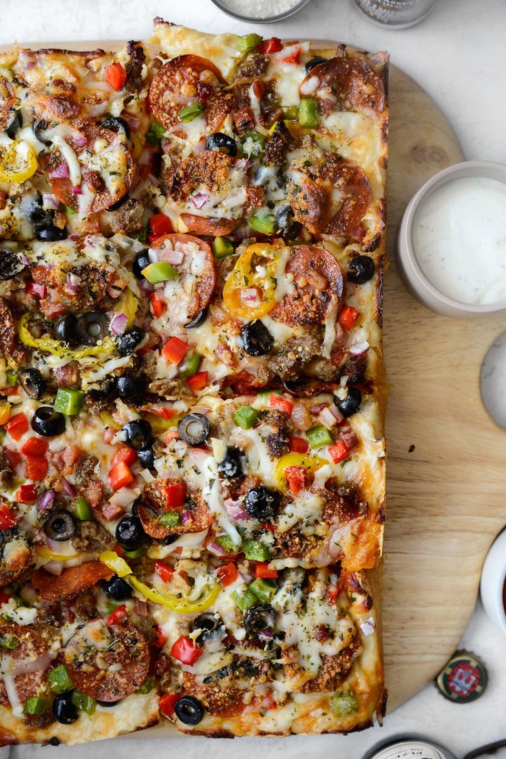 a pizza sitting on top of a wooden cutting board next to cups and sauces