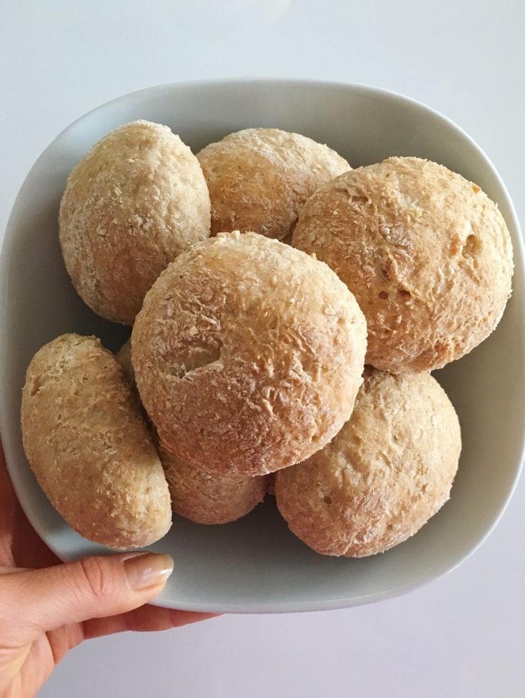 a person holding a bowl filled with doughnuts on top of a white table