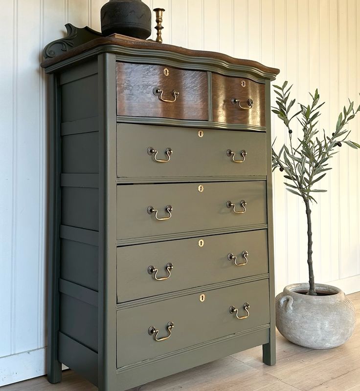 a green dresser with drawers and a potted plant