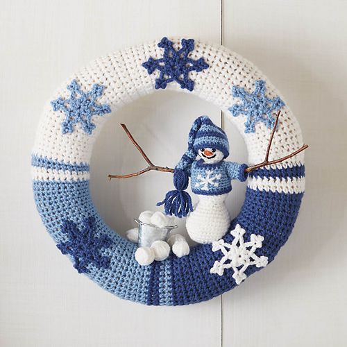 a crocheted snowman wreath hanging on a white wall with blue and white trim