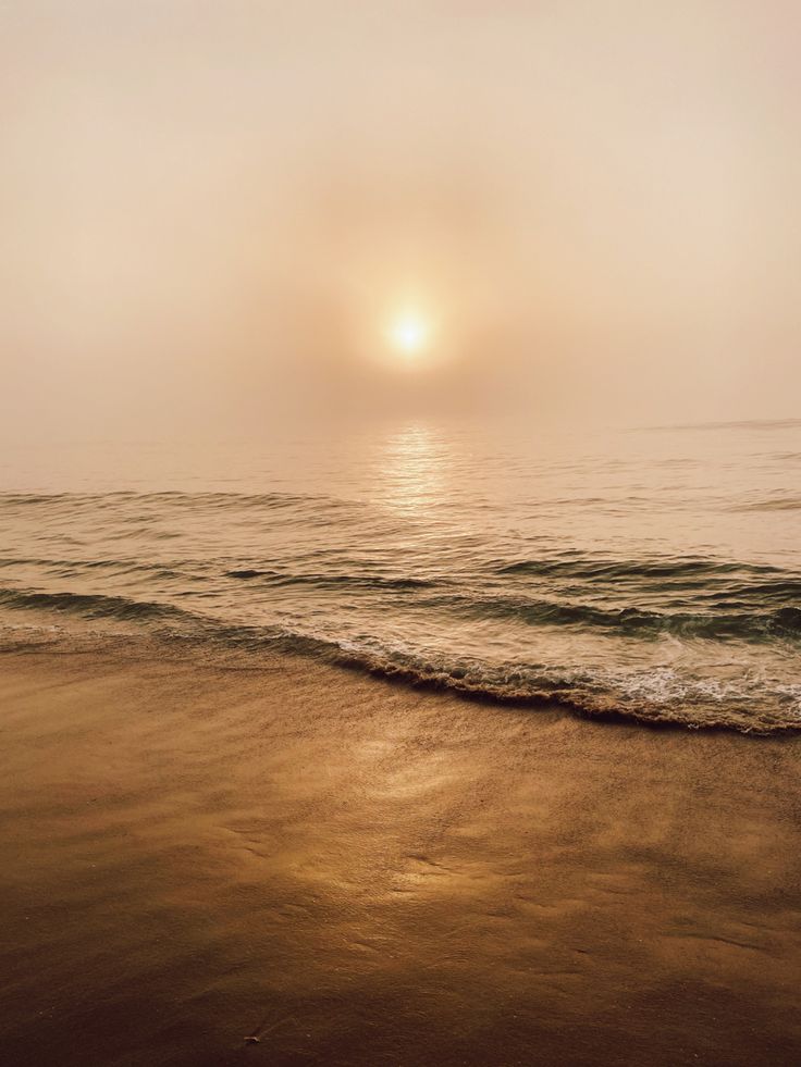 the sun is setting over the ocean with waves coming in to shore and sand on the beach