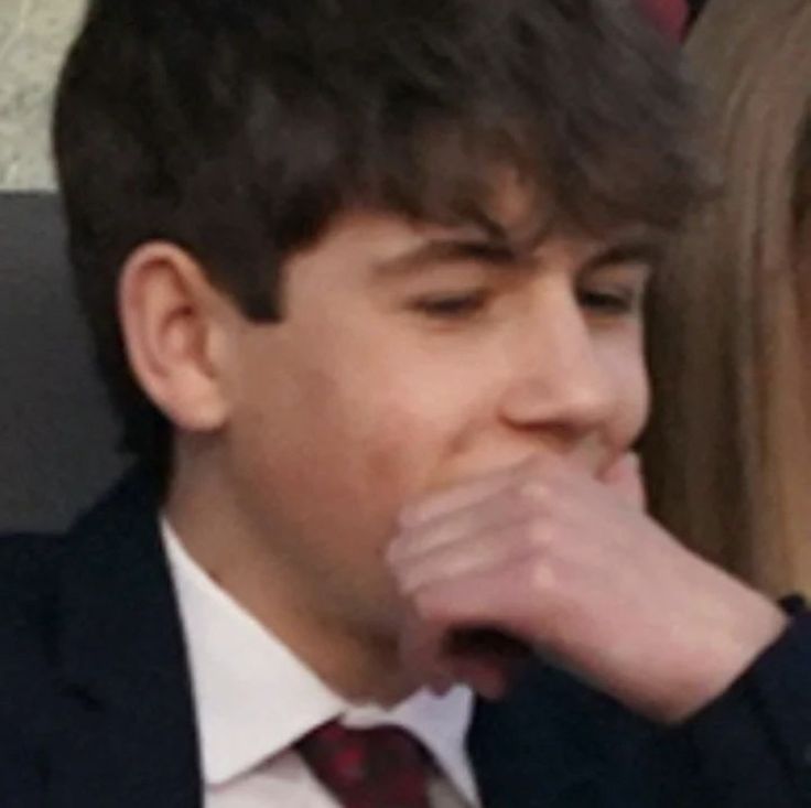 a close up of a person wearing a suit and tie with his hand to his mouth