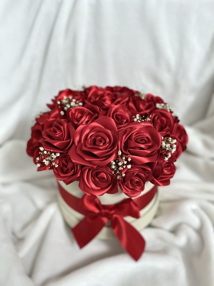 a bouquet of red roses in a white box on a white cloth covered bed sheet