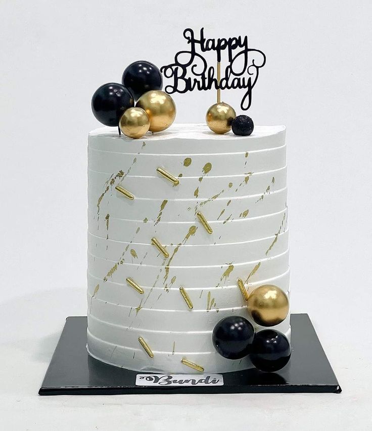 a white and gold birthday cake with black and gold decorations on it's top