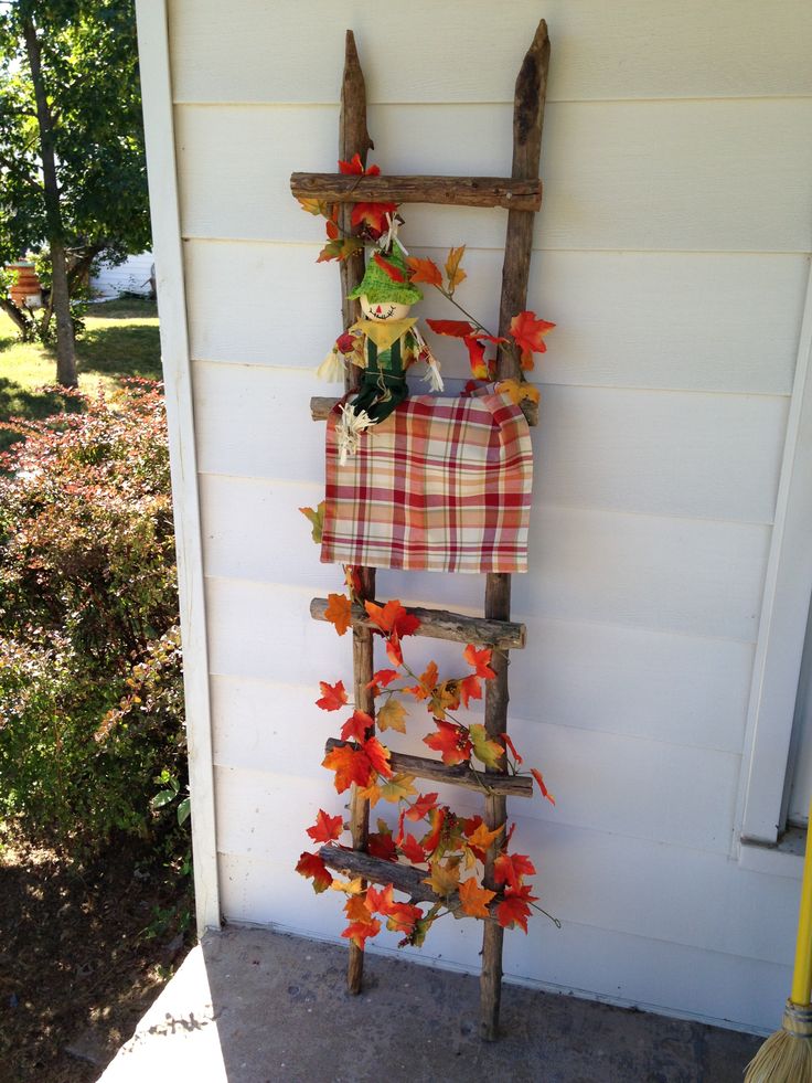 an old ladder is decorated with fall leaves and plaid fabric as well as a scarecrow