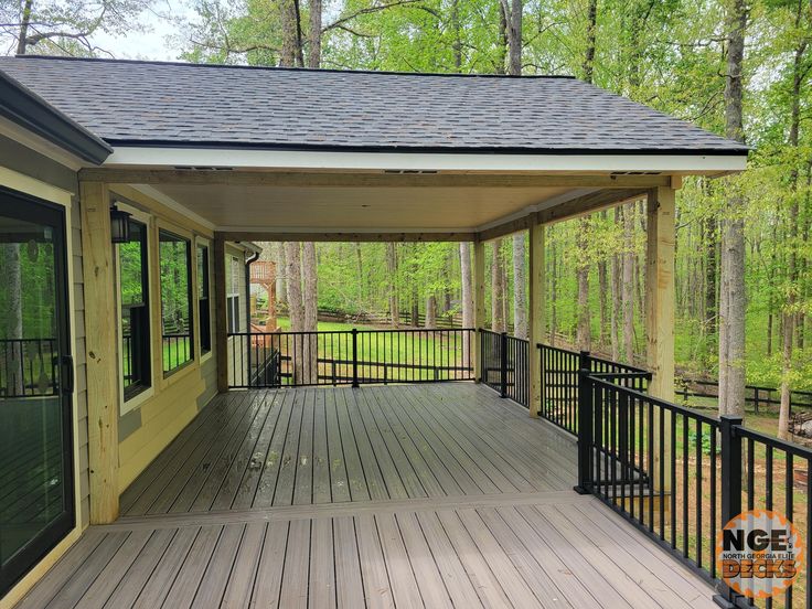 a covered porch with black railing and wood flooring in front of the house, surrounded by trees