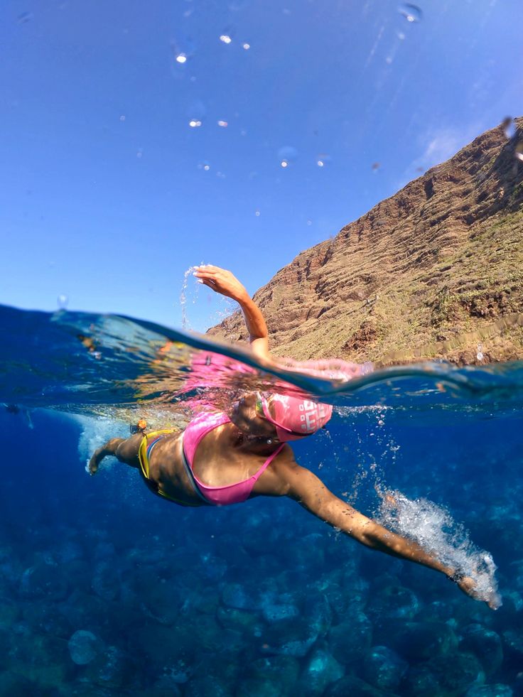 a woman is swimming in the ocean with her arms out and feet up above water