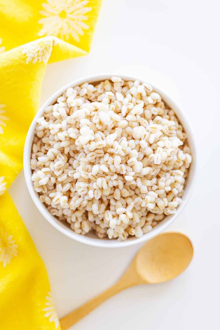 a white bowl filled with brown rice next to a yellow napkin and wooden spoons