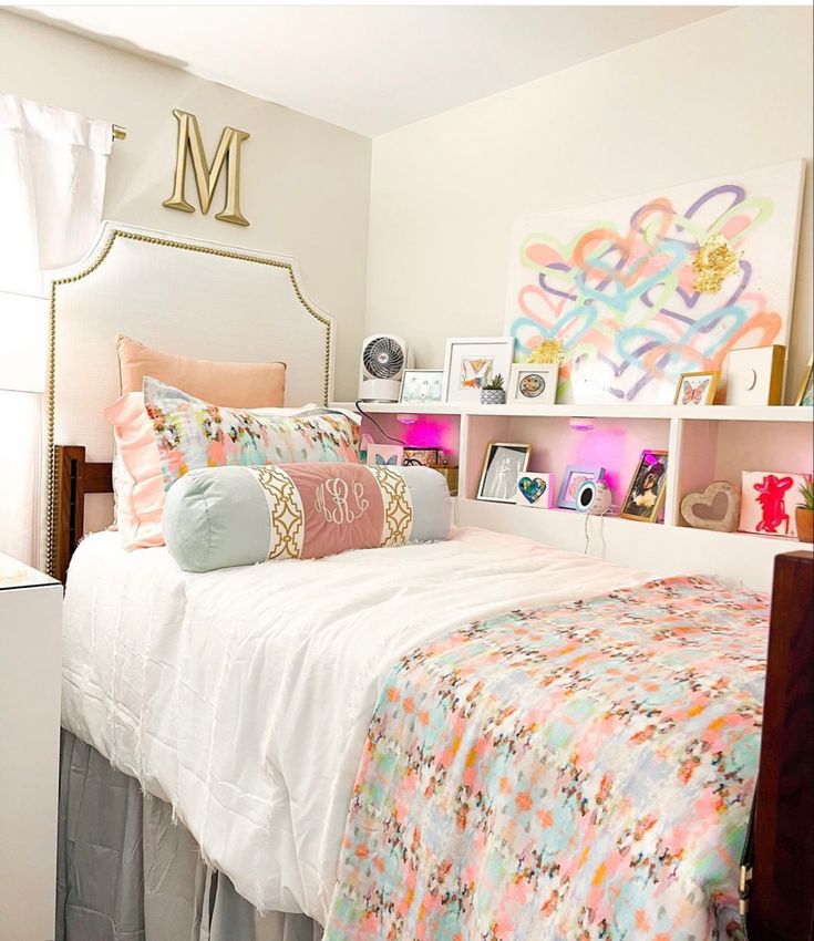 a white bed topped with lots of pillows next to a shelf filled with pictures and other items