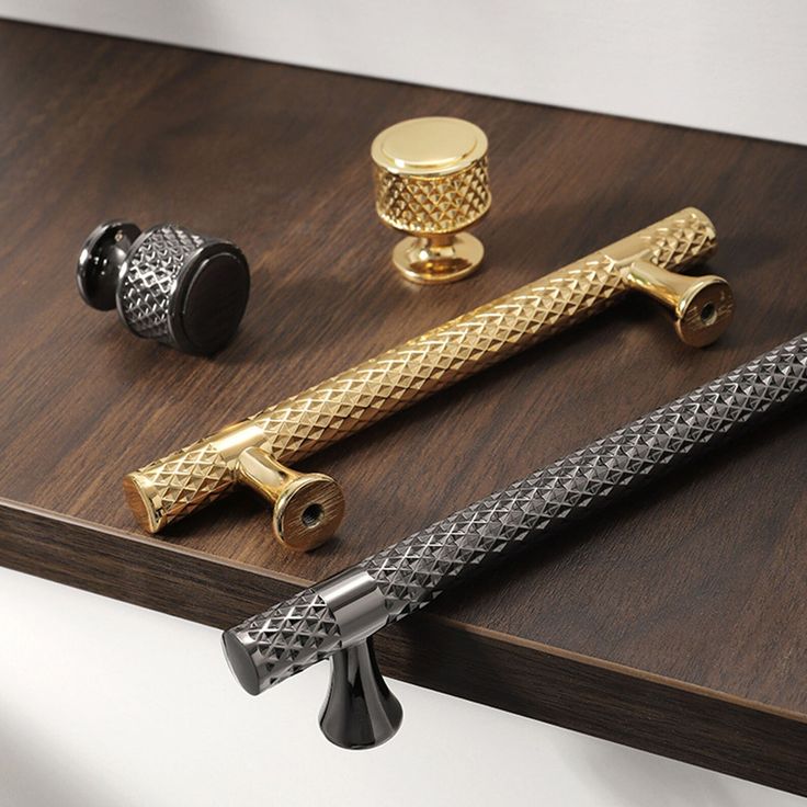 three different types of brass and black handles on a wooden table with two knobs