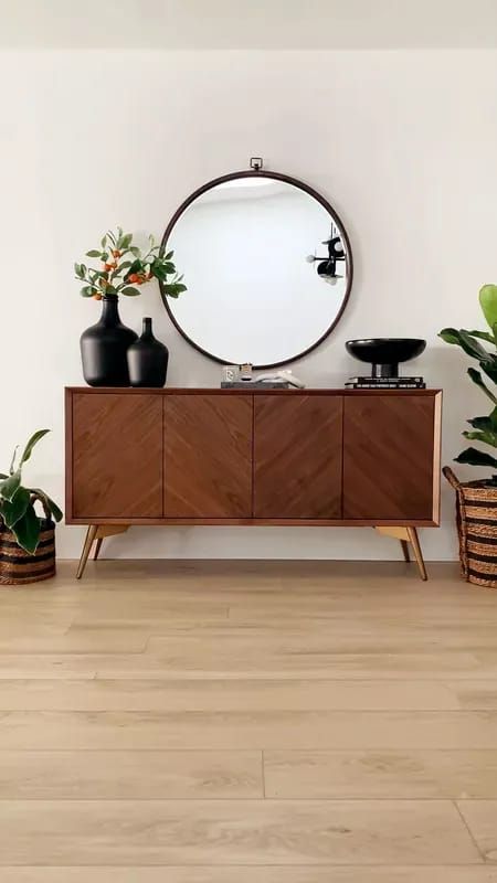 a mirror and some potted plants in front of a white wall with wooden flooring