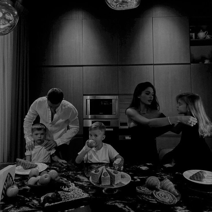 a black and white photo of a family in the kitchen with food on the table