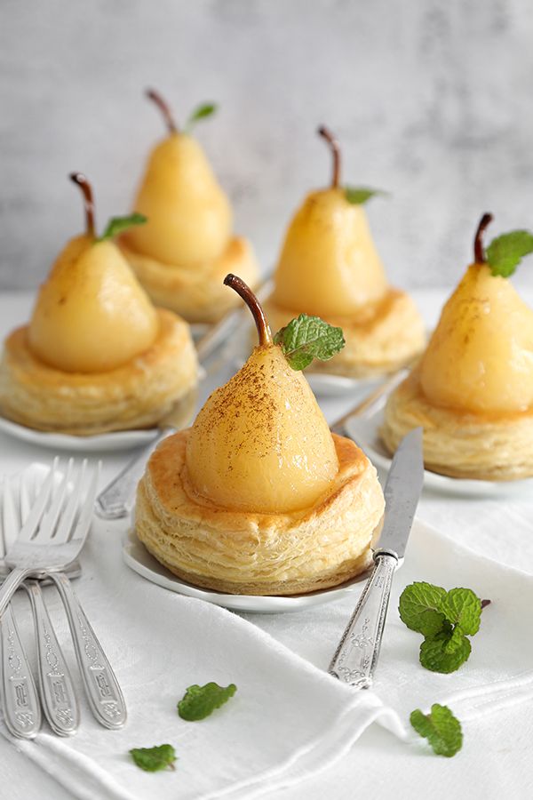 four pear tarts on small white plates with forks and spoons next to them