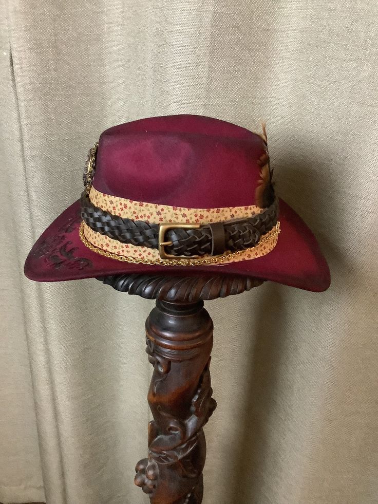 This is a custom weathered hat with incredible detail.  Burgandy felt hat with band of tan fabric with Burgandy flowers. Leather hat band.  Gorgeous broach in front.  Chain ant bottom.  Hat has been wood burned a beautiful scroll design.   Authentic Turkey feathers in back.   Adjustable band inside to fit any size.