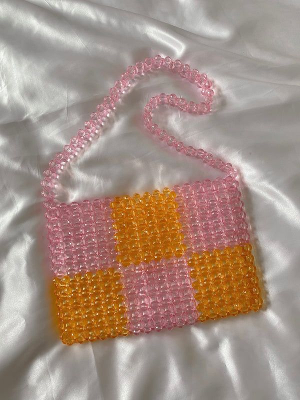 a pink and yellow cross - stitch purse on a white bed with a chain attached to it