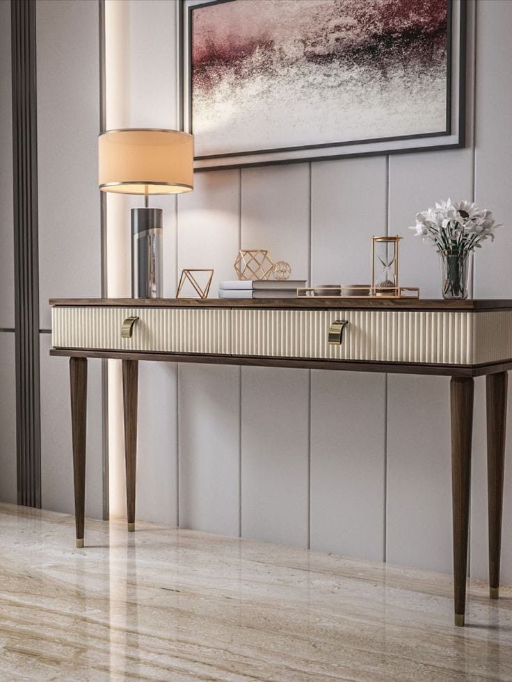 an elegant console table with flowers on it in front of a framed art piece and lamp