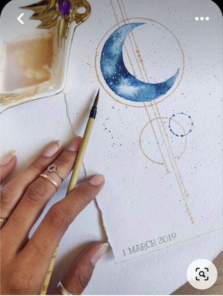 a woman's hand is holding a pencil and drawing a crescent moon on paper