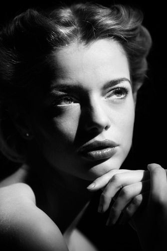 a black and white photo of a woman with her hand on her chin looking at the camera