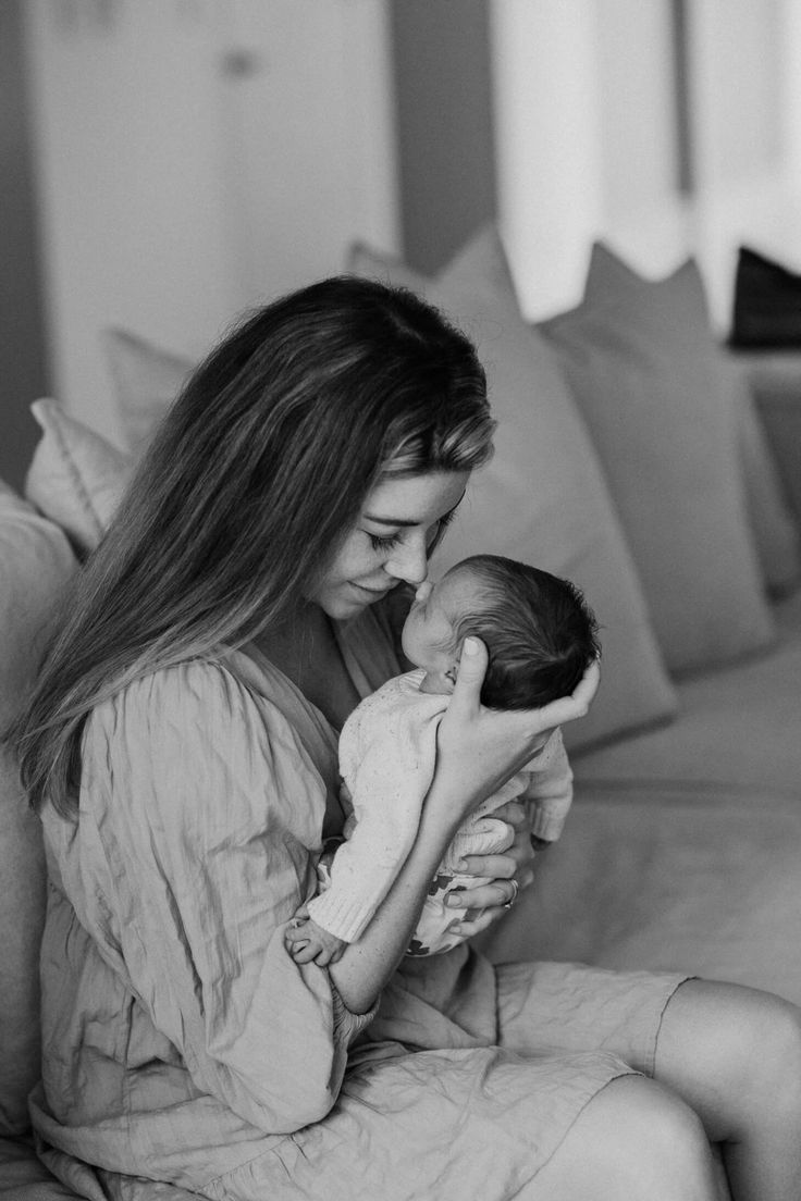 a woman holding a baby while sitting on top of a couch in a living room