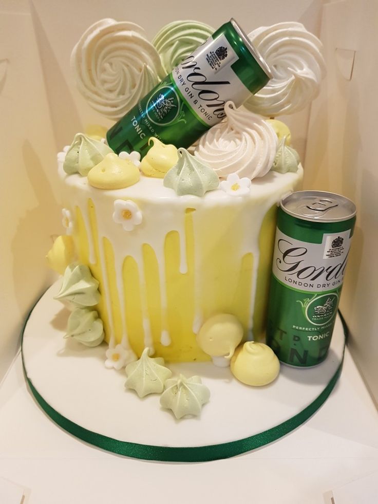 a cake decorated with white icing and candies is on a table next to two cans of soda