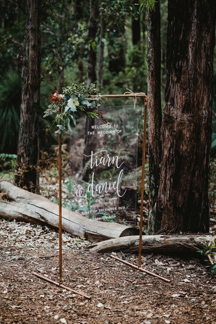 a wedding sign in the woods with greenery and flowers is displayed on an easel