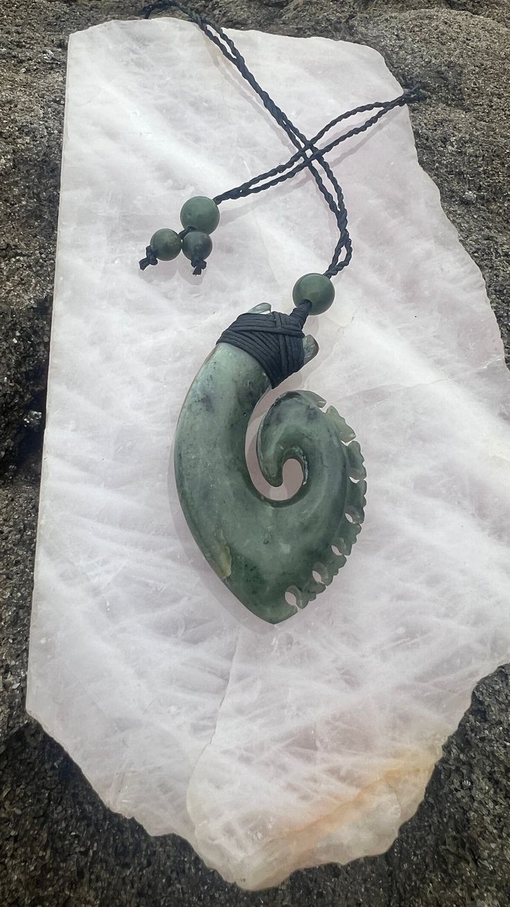 Discover the timeless allure of jade with our Hand-Carved Jade Tribal Fish Hook Necklace. Crafted with meticulous care, this necklace showcases the natural beauty and unique properties of this exquisite gemstone. Jade is renowned for its soothing and protective qualities, believed to bring harmony and balance to its wearer. Each necklace features a hand-carved jade fish hook, symbolizing strength, abundance, and good fortune. Wearing this necklace allows you to carry the calming energies of jade Nature-inspired Jade Pendant Necklace, Traditional Jade Gemstone Necklaces, Traditional Jade Gemstone Necklace, Unique Green Carved Necklace, Nature-inspired Jade Gemstone Necklaces, Nature-inspired Jade Gemstone Necklace, Traditional Jade Jewelry With Natural Stones, Traditional Jewelry With Jade And Natural Stones, Nature-inspired Jade Gemstone Beads Necklace