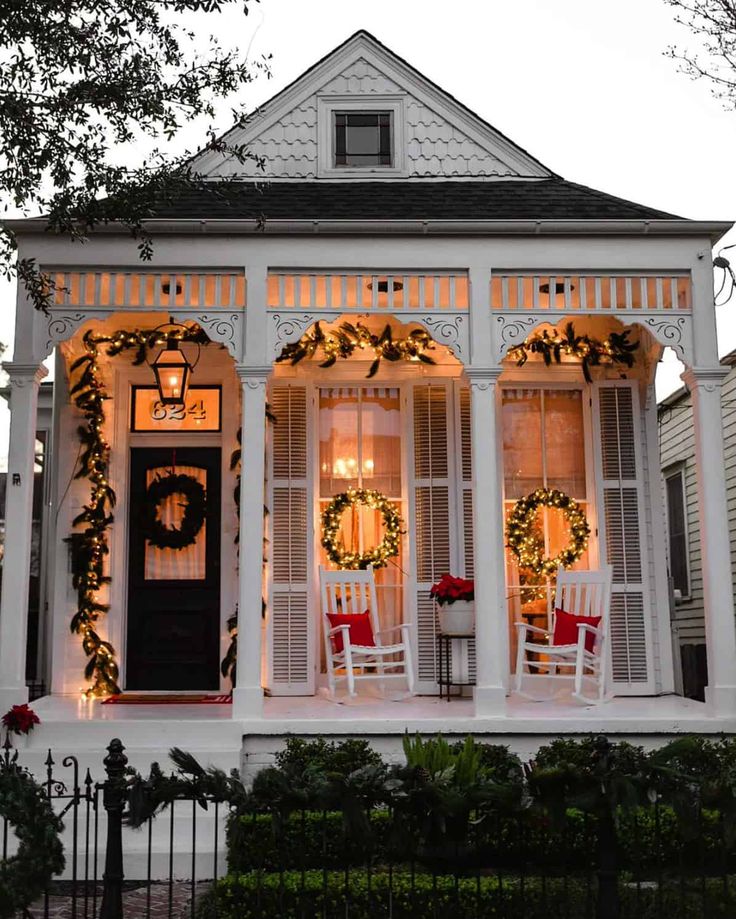 a white house decorated for christmas with wreaths on the front porch and lights hanging from the windows