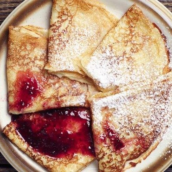 four pieces of crepes on a plate covered in powdered sugar and jelly