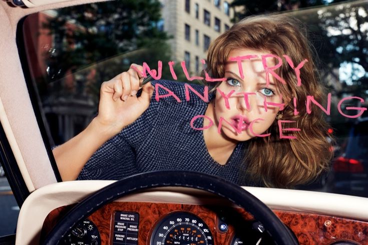 a woman sitting in the driver's seat of a car with pink writing on her face