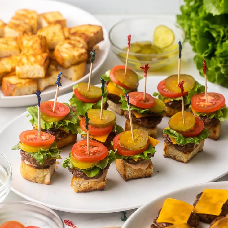 several sandwiches with tomatoes, lettuce and tomato slices on skewers next to potato wedges