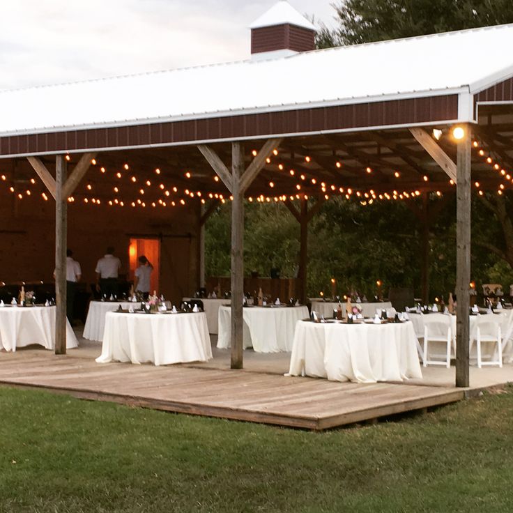 a barn with tables and chairs set up for an outdoor wedding reception in the evening