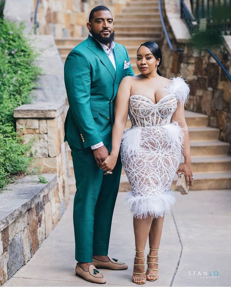 a man and woman standing next to each other in front of stairs wearing green suits